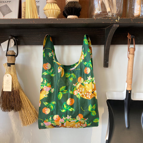 Green Bag with Sleeping Deer Resting on a bed of fruit surrounded by cleaning utensils